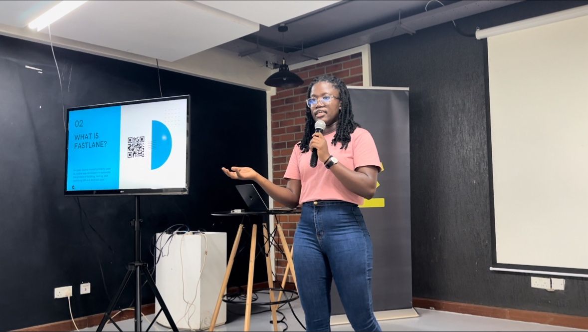 Christine Wasike speaking on stage with a microphone beside a presentation screen